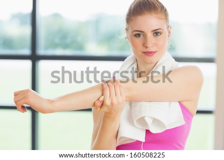 Portrait of a young woman with towel around neck stretching hand in fitness studio