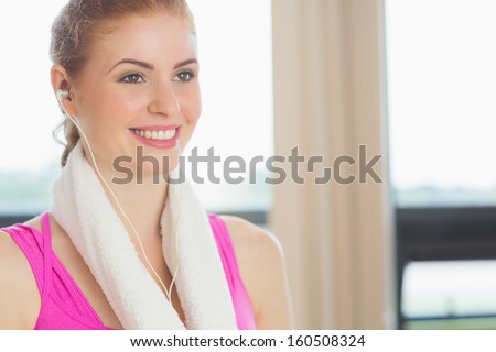 Close-up of a smiling woman with towel around neck listening to music in fitness studio
