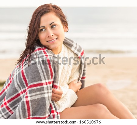 Beautiful young woman covering herself with blanket at the beach