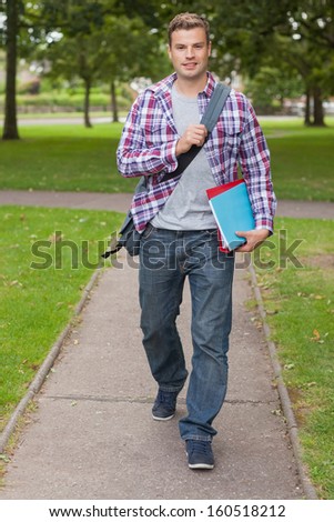 Handsome happy student carrying notebook and folder on campus at college