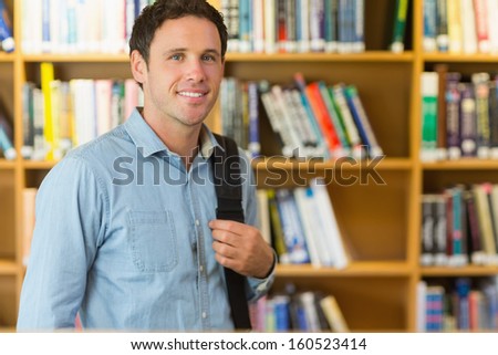 Portrait of a smiling mature student with bag against bookshelf in the library