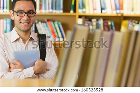 Portrait of a smiling mature student with tablet PC against bookshelf in the library