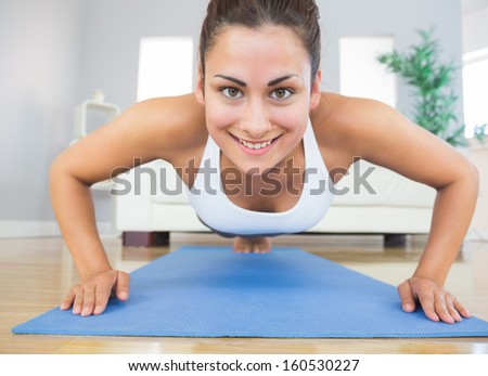 Fit young woman practicing press ups on a blue exercise mat in her living room