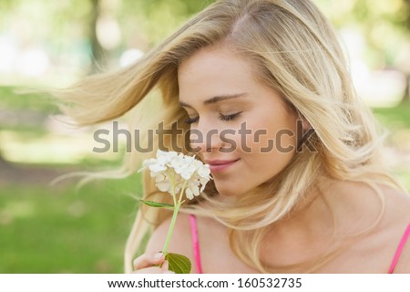 Gorgeous content woman smelling a flower with closed eyes sitting on a lawn