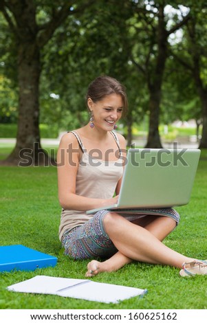 Smiling female student using laptop with books at the park
