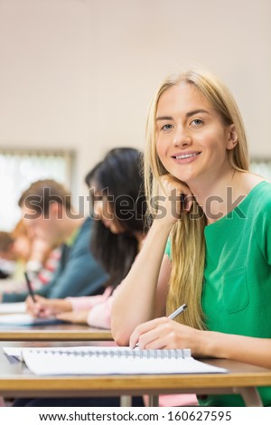 Portrait of a young female student with others writing notes in the classroom