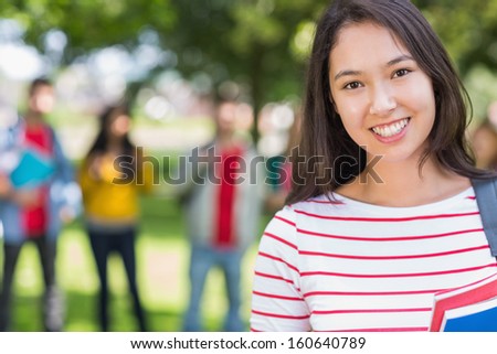 Close-up portrait of college girl with blurred students standing in the park