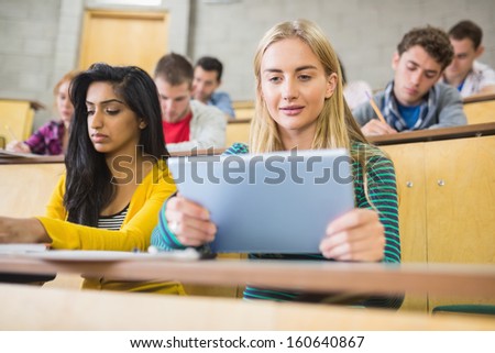 Young female using tablet PC with students at the lecture hall