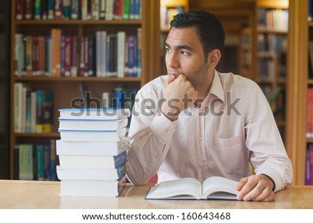 Attractive man sitting in library in front of an opened book looking thoughtful out of the window
