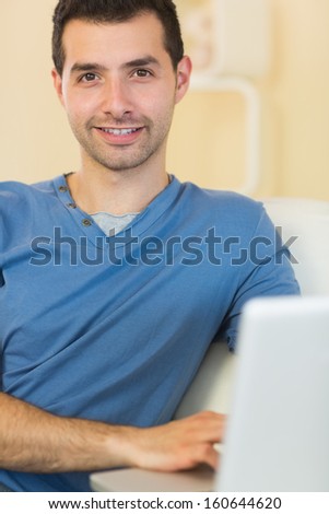 Casual happy man sitting on couch using laptop in bright living room
