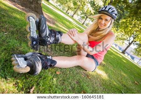 Casual cheerful blonde wearing roller blades and helmet in a park