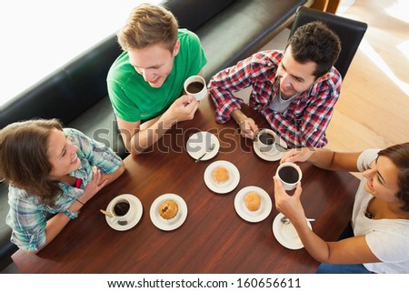 Four smiling students having a cup of coffee chatting in college canteen
