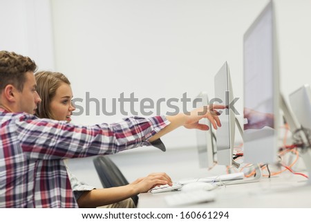 Two students working on computer pointing at it in computer room at college