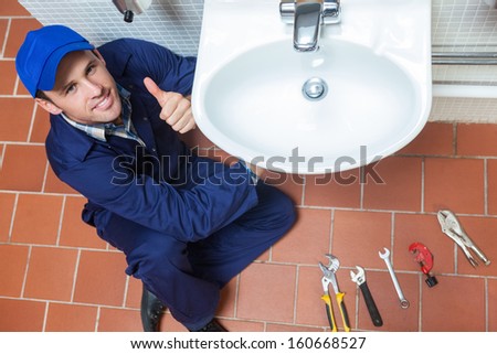 Smiling plumber repairing sink showing thumb up in public bathroom