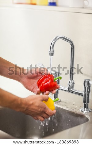 Kitchen porter washing vegetable under running tap in professional kitchen