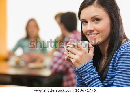 Portrait of a smiling female having coffee with students around table in background at  the coffee shop