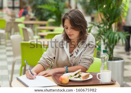 Female student doing homework while having breakfast in the cafeteria