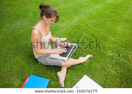 Side view of a female student using laptop with books at the park