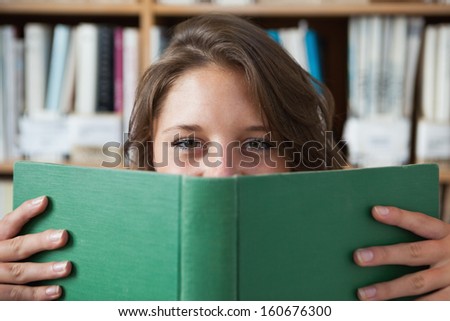 Close-up portrait of a female student holding book in front of her face in the library