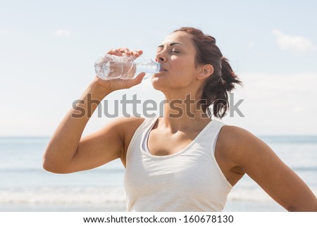 Content beautiful woman drinking of water bottle standing on the beach