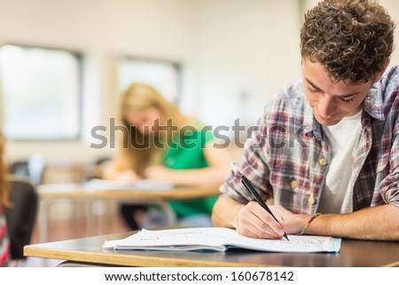 Young male student with others writing notes in the classroom