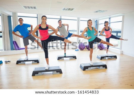 Full length portrait of instructor with fitness class performing step aerobics exercise in gym