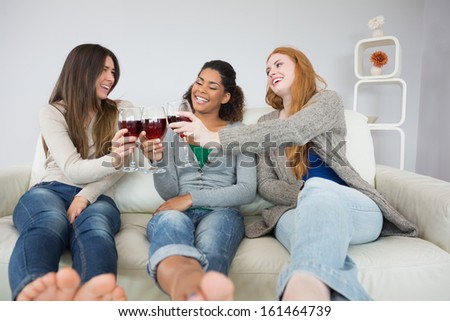 Cheerful young female friends toasting wine glasses on sofa at home