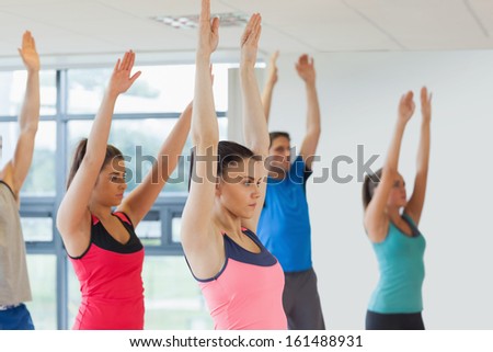 Side view of sporty people raising hands at yoga class in fitness studio