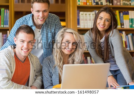 Group portrait of four happy students using laptop at desk in the college library