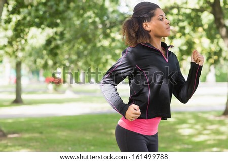 Side view of a beautiful healthy young woman in black jacket jogging in the park