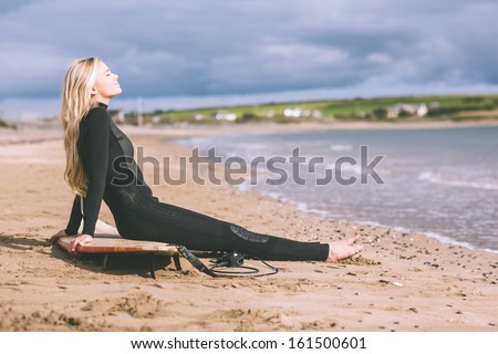 Side view of a beautiful blond in wet suit with surfboard at the beach