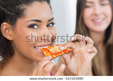 Close up portrait of a young female eating pizza with blurred friend at home