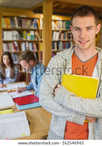 Portrait of a smiling male student with others in background in the college library