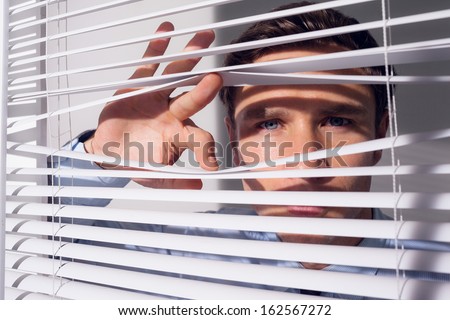 Close up portrait of a young businessman peeking through blinds