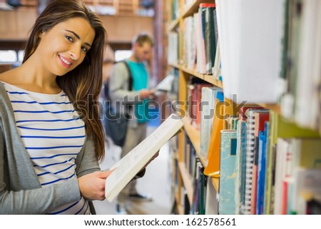 Side view portrait of two young students standing by bookshelf in the library