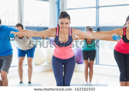 Full length of instructor with fitness class performing step aerobics exercise with dumbbells in a gym