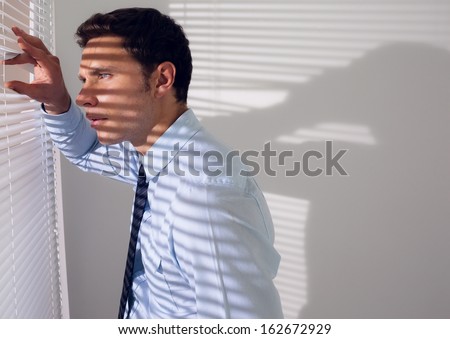 Side view of a young businessman peeking through blinds in office