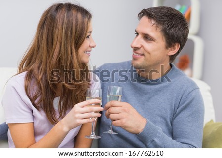 Romantic smiling young couple toasting flutes in the living room at home