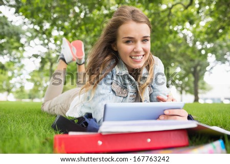 Smiling student lying on the grass studying with her tablet pc on college campus