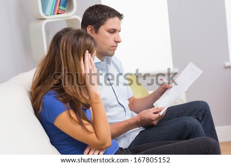 Stressed couple sitting on couch and paying their bills in the living room at home