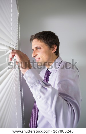 Side view of a young businessman peeking through blinds in the office