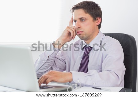 Young worried businessman using laptop at desk in the office