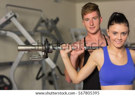 Portrait of a young male trainer helping young fit woman to lift the barbell in the gym