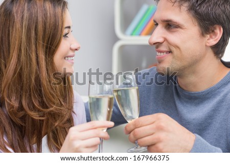 Close-up of a smiling young couple toasting flutes in the living room at home