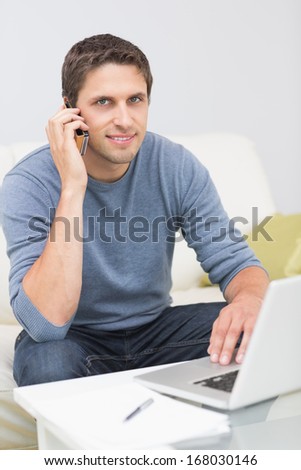 Portrait of a smiling young man using cellphone and laptop in the living room at home