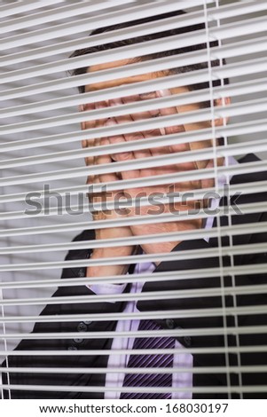 Young businessman standing with head in hands in front of blinds in the office