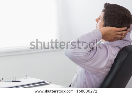 Thoughtful relaxed businessman sitting with hands behind head in the office