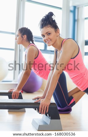 Side view of two fit women performing step aerobics exercise in gym