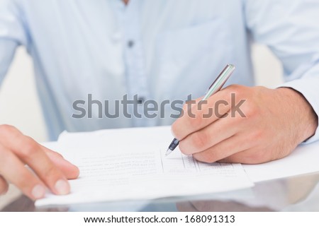 Close-up mid section of a young man writing documents at the table