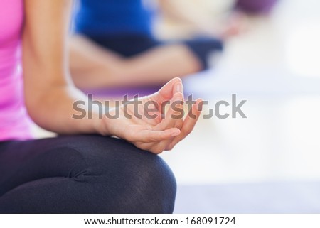 Close-up of cropped sporty women in lotus pose at a bright fitness studio